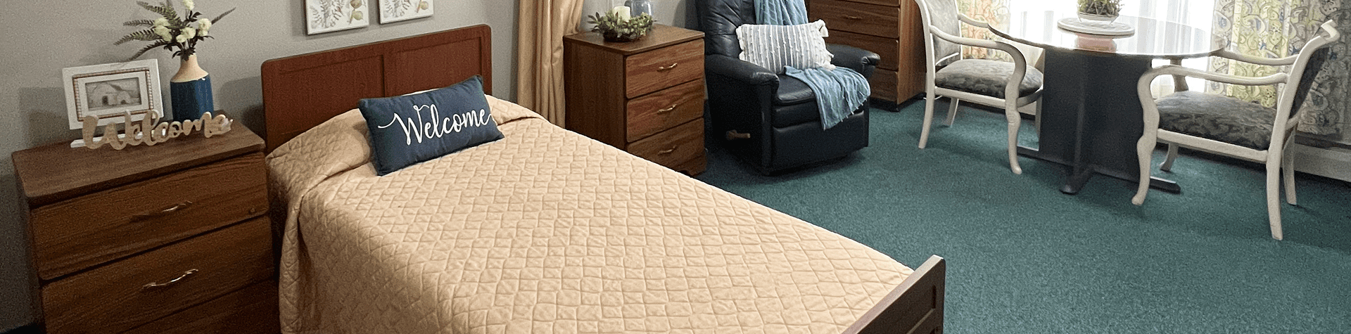 A cozy bedroom with a wooden bed frame and a beige quilt, decorated with a navy blue pillow with 